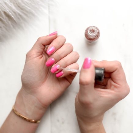 person spreading glittered nail polish on pink nails