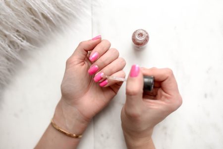 person spreading glittered nail polish on pink nails